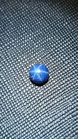 Blue star sapphire cabochon exhibiting a strong 6-ray star reflection on a textured dark background.