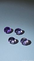 Four oval purple amethysts arranged on a flat surface under lighting to show facets and clarity.