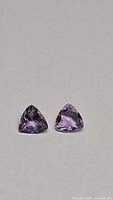 Top view of two natural Brazilian amethyst gemstones showing purple color and trillion cut shape.