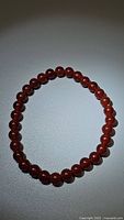 Clear image showing natural carnelian beads arranged in a circular bracelet shape on a white background.