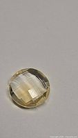 Close-up image of round, pale yellow citrine gemstone showing double-sided fancy cuts and minor internal inclusions.