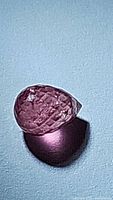 Close-up image of a pinkish-red natural ruby gemstone with fancy briolette cut, showing multiple facets and drilled hole for jewelry use.