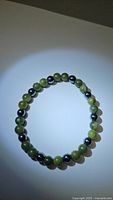 Full view of the bracelet laid flat showing alternating green jade and dark hematite beads.