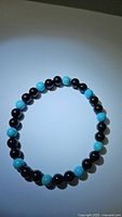 Bracelet with alternating shiny black onyx and bright robin's egg blue turquoise beads, laid flat in circular form on light background.