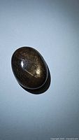 Natural oval cabochon golden sheen sapphire on a neutral background, showing reflection and sheen.