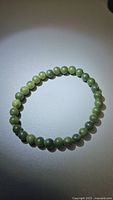 Photo showing a natural green jade bead bracelet with uniformly sized 6mm round beads arranged in a circle on a white surface, lit from above.