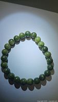 Full view of circular green jade bead bracelet under focused light showing color variations and shine on beads.