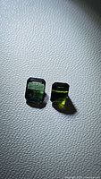 Two natural, untreated green tourmaline gemstones shown on textured surface under bright light showing clarity and color