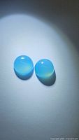 Two round cabochon icy blue chalcedony gemstones on a white background, showing translucent qualities and smooth polished surfaces.