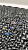 Nine oval cabochon labradorite stones with blue flashes on textured black fabric background