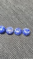 Four round cabochon Lapis Lazuli beads on black textured background showing color and surface details.