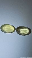 Two oval cabochon lemon citrine gemstones side by side on a plain white background showing translucence and deep yellow color, photographed in natural light.