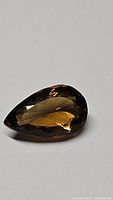 Close-up photo of a pear cut Madeira citrine gemstone showing its faceted surfaces and deep cognac color on a grey background.