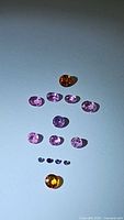 Natural sapphire stones laid out on light background, showing pink, purple, and orange colors, mixed cuts and sizes.