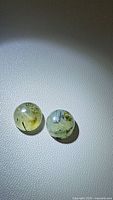 Pair of natural moss agate oval cabochons with visible moss inclusions on a white textured surface.