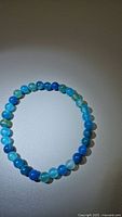 Photo of round ocean blue agate bead bracelet on a light surface showing bead colors and bracelet shape.