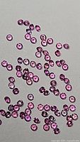Multiple natural pink sapphires scattered on a neutral surface showing round, deep pink, faceted stones with diamond-style cuts.