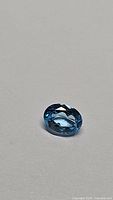 Close-up photo of single oval shaped natural Swiss blue topaz gemstone with bright lagoon-blue color and faceted cut.