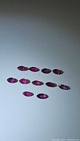 Photo showing 10 marquis cut ruby gemstones laid out on a flat surface with visible vibrant red coloration and good clarity.