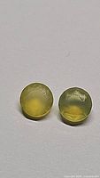 Two round cut yellow fire opal gemstones on a plain background, showing color and cut details.