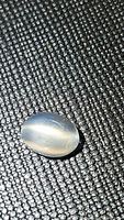 Oval cabochon natural catseye moonstone on textured black surface, showing horizontal catseye effect and polished smooth finish.