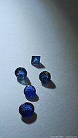 Photo of five natural royal blue sapphires on white background, showing cut shapes and color.
