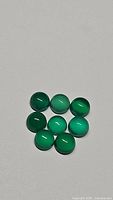 Nine round vivid green Onyx cabochon gemstones arranged closely on a white background, showing color and surface quality.