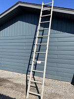Full view of 12 foot aluminum ladder leaning upright against a house wall outdoors on gravel ground