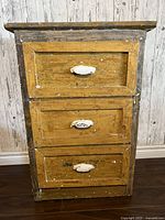 Front view of antique wood cabinet with three drawers and white painted cast iron pulls showing distressed finish.