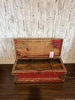 Open antique wooden carpenter's tool chest showing interior compartments and lid with original red paint and wear.