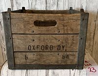 Side view of wooden milk crate with metal reinforcements, showing 'OXFORD DY 5 64' stamped on the wood.