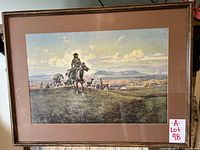 Framed art print by Charles Marion Russell showing a cowboy and horse riders in a western landscape, on wall with a radiator below. Frame is wood with glass, matting is brown.