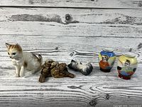 Five figurines including white/orange ceramic kitten, brown resin baby birds, white/grey lying kitten, and two small oriental vases with painted scenes.