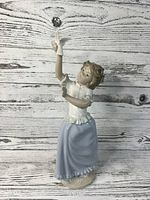 Front view of porcelain figurine showing girl holding a white dove on raised arm, detailed clothing, and facial features