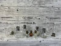 Lot of seven oil lamps of two different sizes arranged in a row, with visible chimneys and metal wick holders on a wooden plank background.