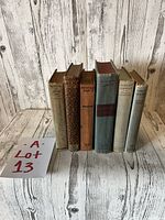 Front view of six old books aligned vertically showing their front covers and thickness.