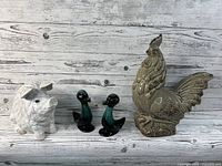 Lot of four animal figurines: resin pig, ceramic rooster, pair of ceramic ducks all shown on wooden background