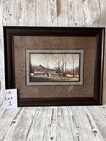 Framed art print with dark wood frame and multi-layered mats showing a rural barns scene by Ray Hendershot, photographed against a wood plank backdrop.