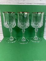 Front view of three vintage stemmed crystal glasses with gold rims against a white wood and green background.