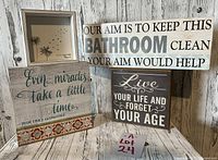 Four assorted word art pieces styled on a wooden backdrop including dandelion art, bathroom cleanliness sign, motivational and fairy tale themed quotes.