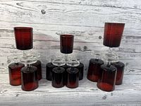Fourteen vintage cranberry glass drink glasses with clear stems arranged upright and upside down showing size comparison.