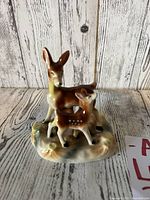 Front angle view of the vintage porcelain doe and fawn figurine on a rustic wooden background.