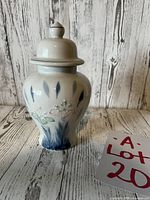 Front view of vintage Japanese hand painted ginger jar with lid, showing floral and leaf design, placed on wood background.