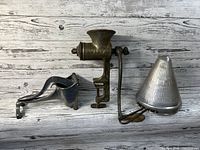 All three vintage kitchen tools arranged on distressed wooden plank background: aluminum juicer, cast iron grinder, aluminum cone strainer