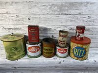All eight vintage kitchen tins grouped together on a wooden surface with whitewashed wood panel background.