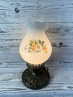 Vintage milk glass hurricane lamp showing floral pattern on the shade with scalloped top and ornate metal base.