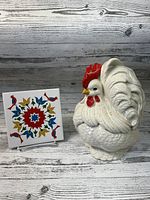 Trivet and rooster cookie jar together against a wood plank background, showing both items clearly