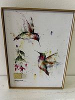 Front view of the framed canvas print depicting hummingbirds and floral design with artist signature and gold emblem.