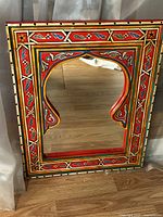 Front view of the painted wooden oriental mirror showing detailed colorful designs and wooden frame with arched top cutout around mirror glass.
