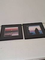 Pair of two black framed art prints positioned side by side on a white surface against a wall